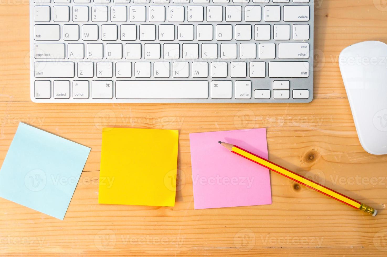 arbetsyta ovanifrån med färgglada klisterlappar, penna, tangentbord och mus på träbordsbakgrund. foto