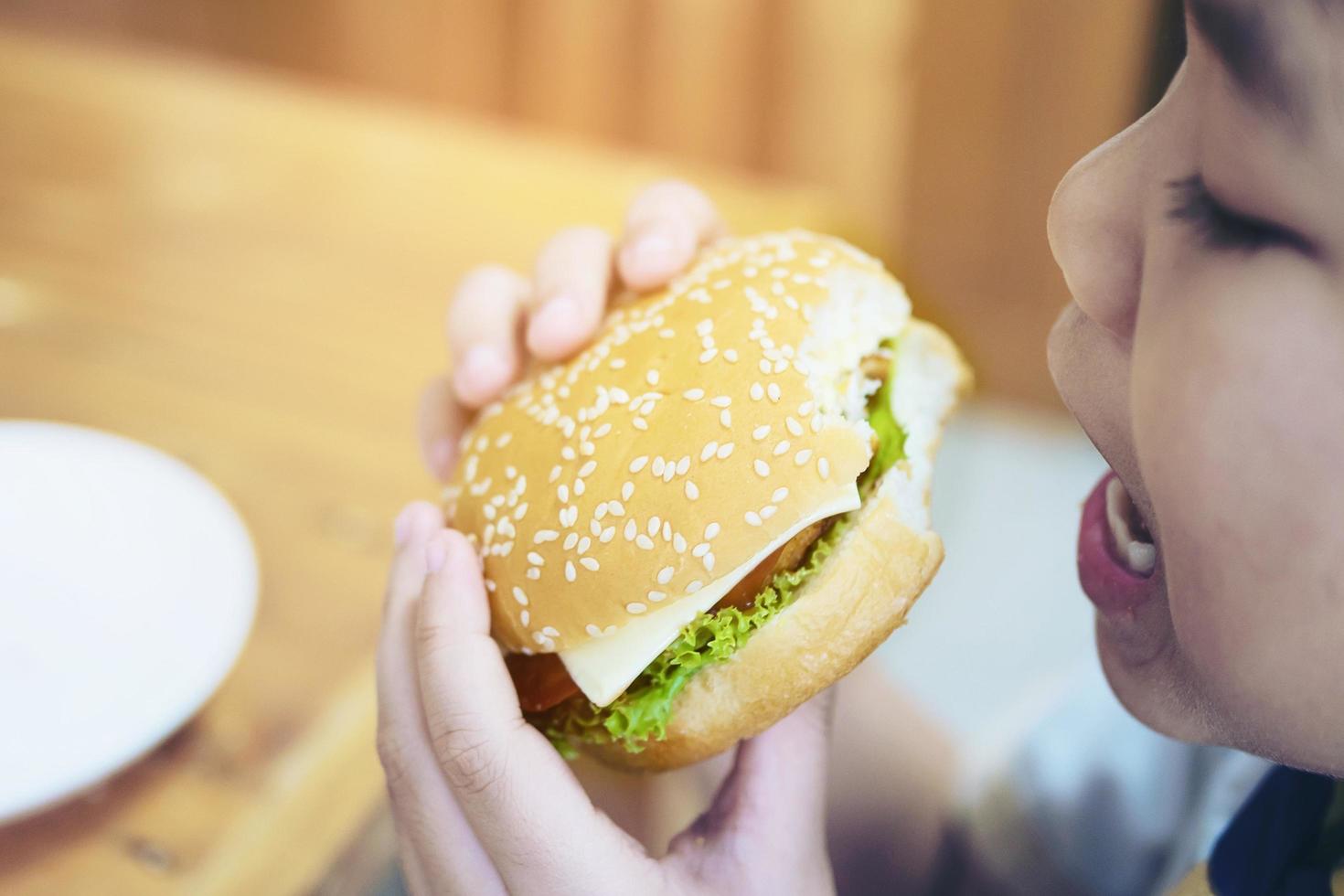 pojke äter hamburgerfrukost med oskärpa träbordsbakgrund - utsökt snabbmatsfrukostkoncept foto