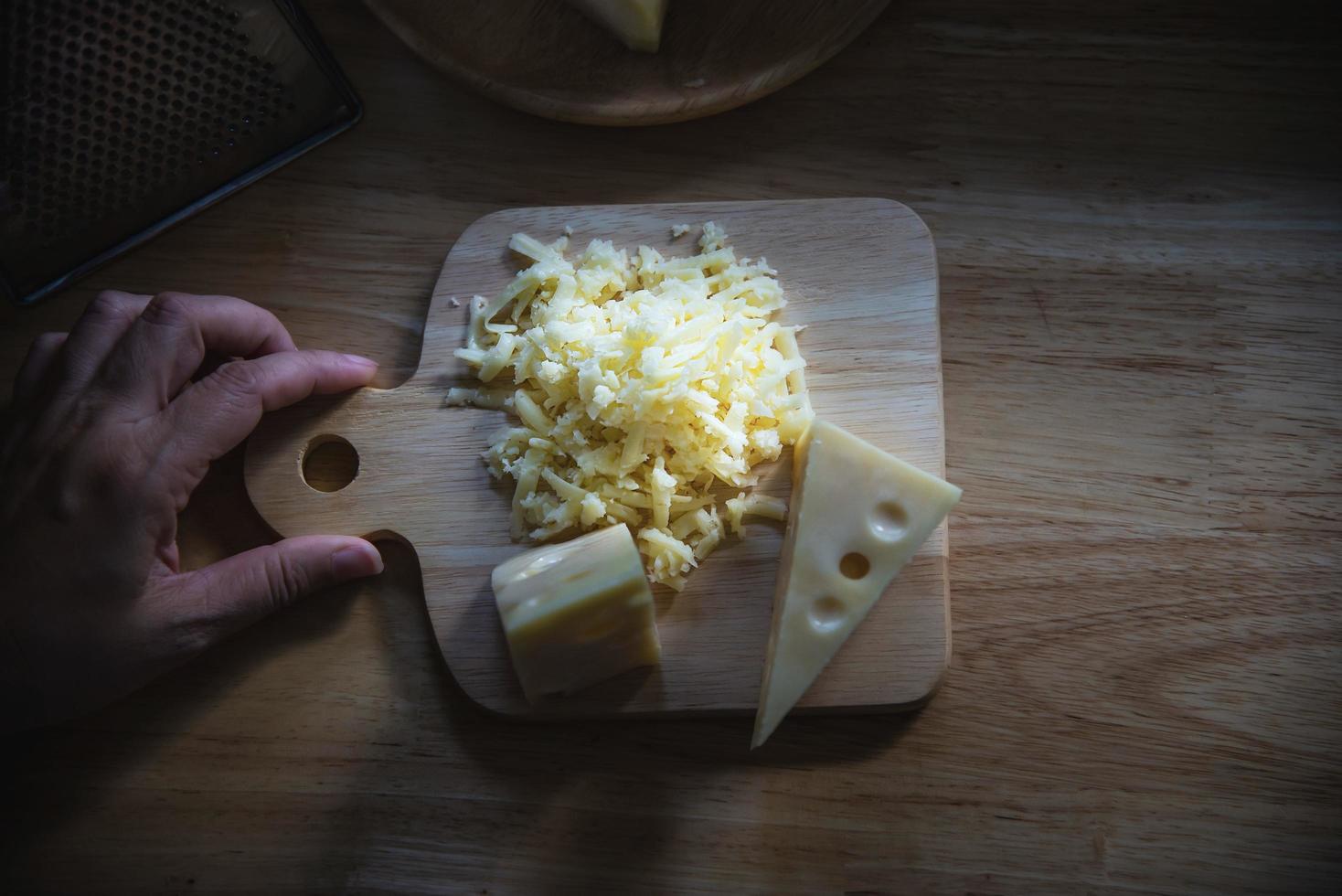 kvinna som förbereder ost för kock med ostrivjärn i köket - människor som gör mat med ostkoncept foto