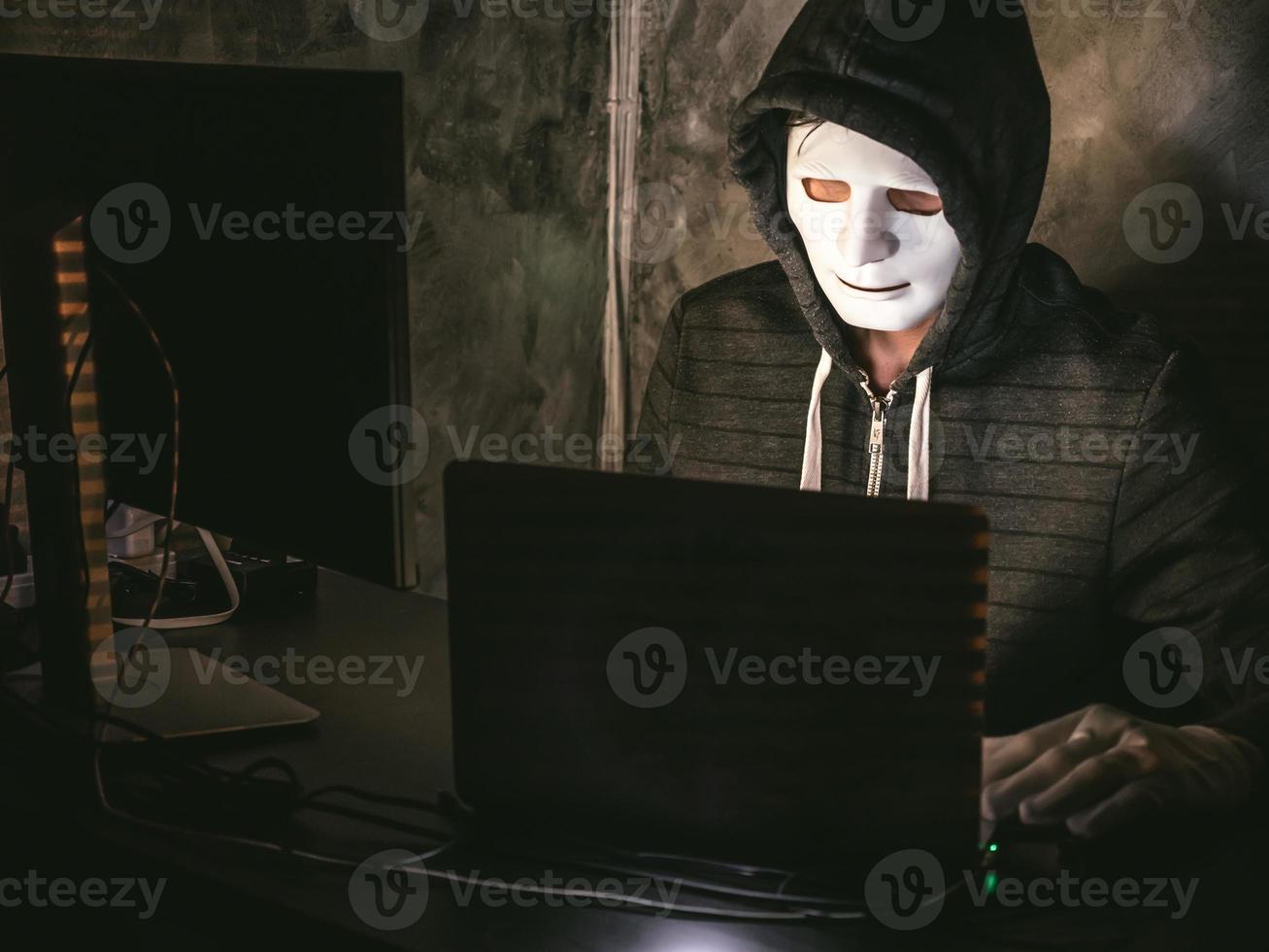 datorhacker - man i huvtröja med mask stjäl data från laptop foto