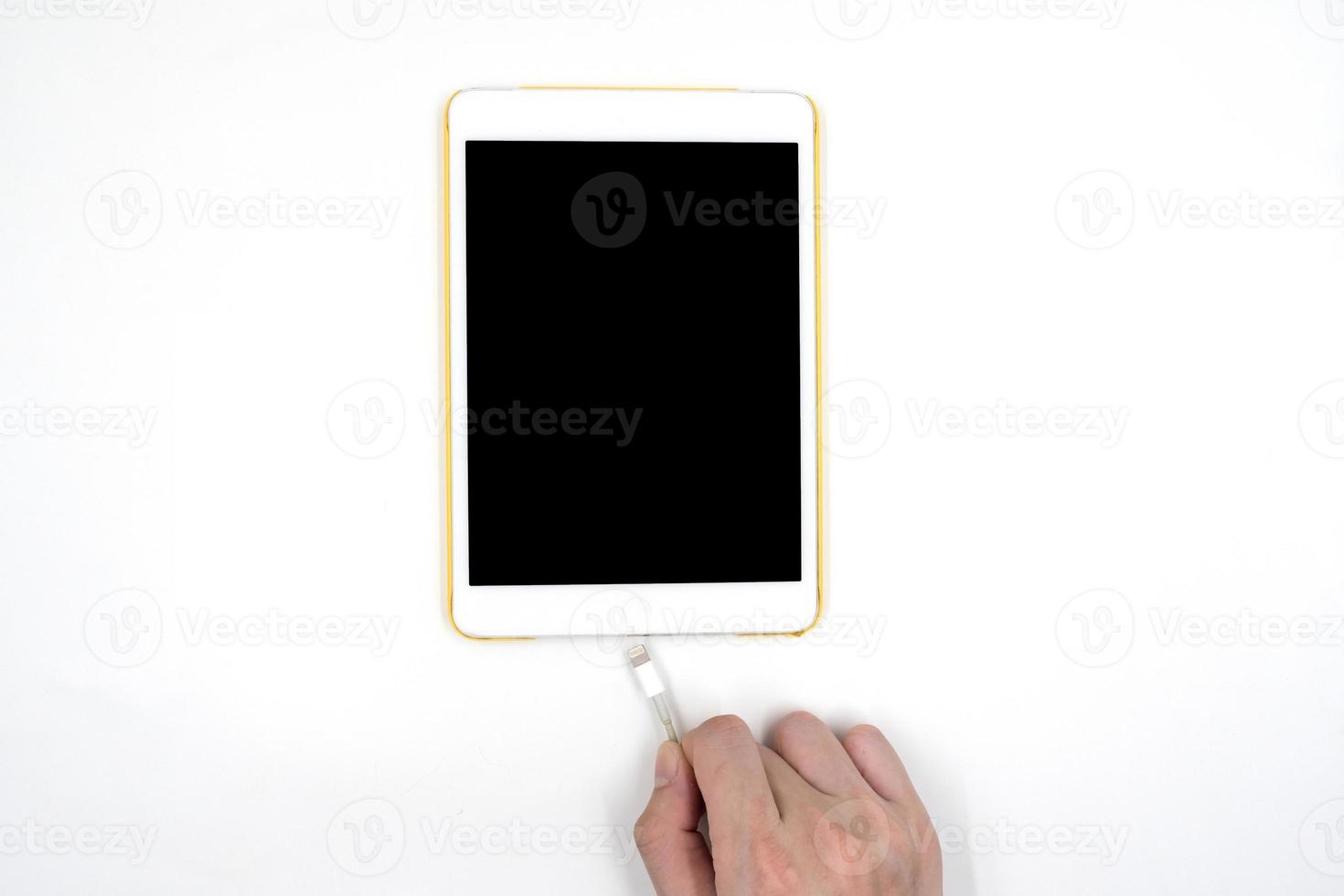 manlig hand som håller usb-kabel med en vit surfplatta touch dator gadget med touch tom svart skärm isolerad på vit bakgrund. foto