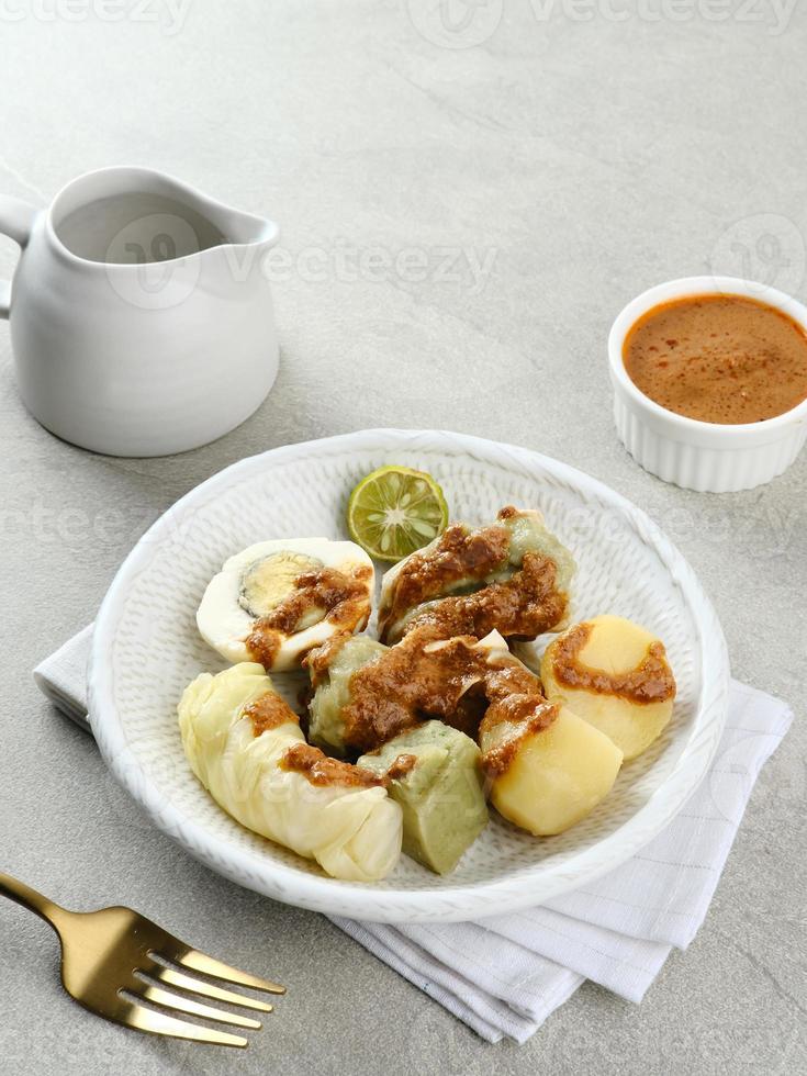 siomay bandung, ångade klimpar med kokt ägg, tofu, potatis och kålrulle. indonesisk traditionell gatumat med jordnötssås och sojasås, serverad med grön lime. foto