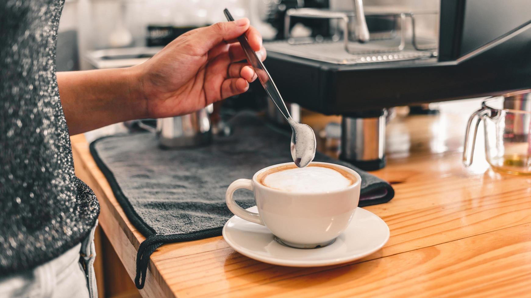 professionell barista använd en rostfri sked för att jämna ut mjölkskum i en varm kaffekopp för att göra cappuccino eller latte på kaféet hur man gör latte art av barista i mjölk och kaffe. foto