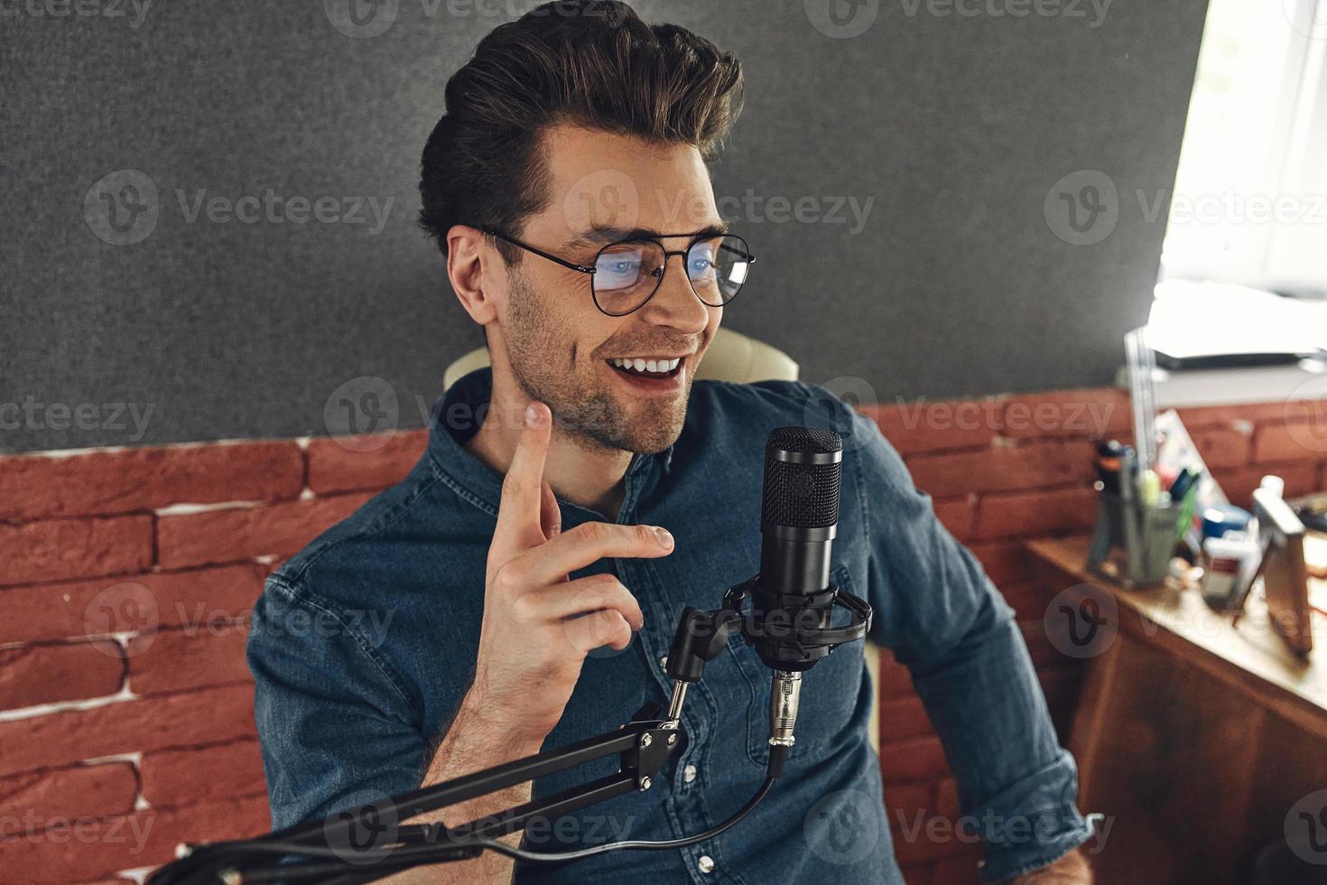 glad ung man använder mikrofon och gester medan du spelar in podcast i studio foto