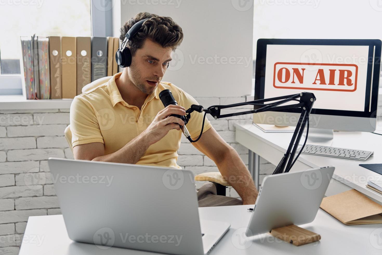 självsäker ung man använder mikrofonen medan du spelar in podcast i studio foto