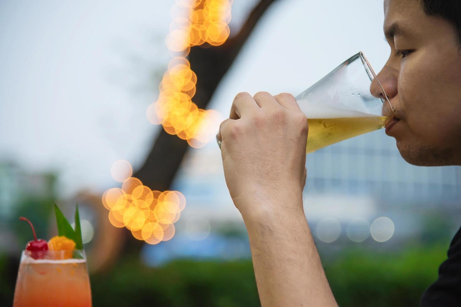 asiatisk man dricker öl i grön trädgårdsrestaurang - människor kopplar av och njuter av läsk livsstilskoncept foto