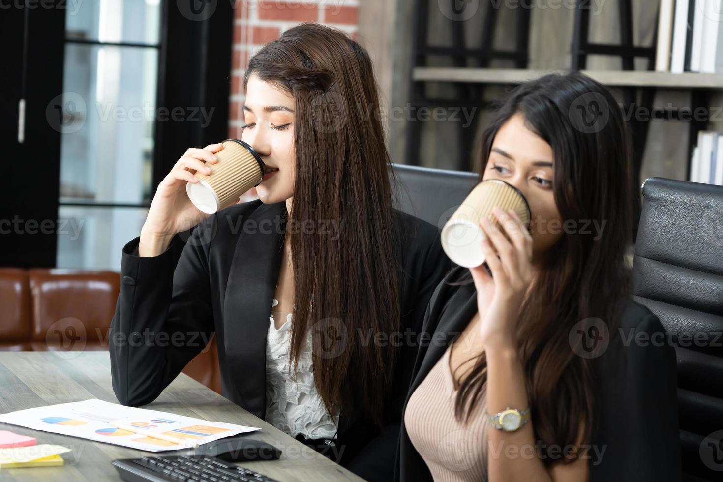 kontorsfika med två kvinnliga kollegor som sitter och pratar över koppar kaffe. asiatisk affärskvinna med kaffekopp på kontoret. foto