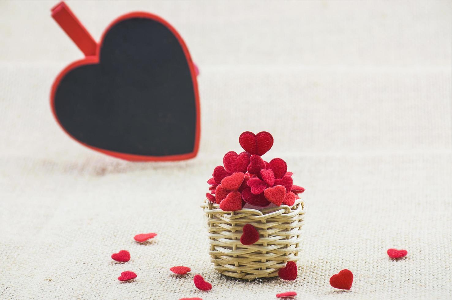 hjärtan i liten trävävkorg och ett kärleksord på en hjärttavla som sätter på säcktyget. foto