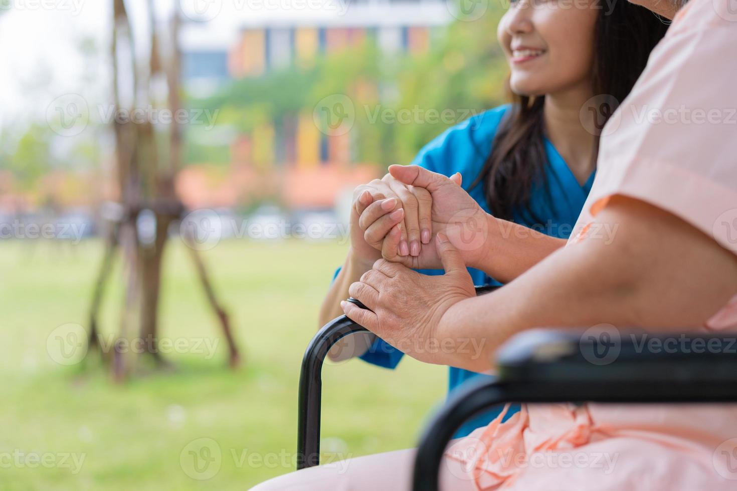 asiatisk omsorgsfull vårdgivare eller sjuksköterska håller patientens hand och uppmuntrar patienten i rullstol. begreppet lycklig pensionering med omsorg från en vårdgivare och sparande och senior sjukförsäkring. foto