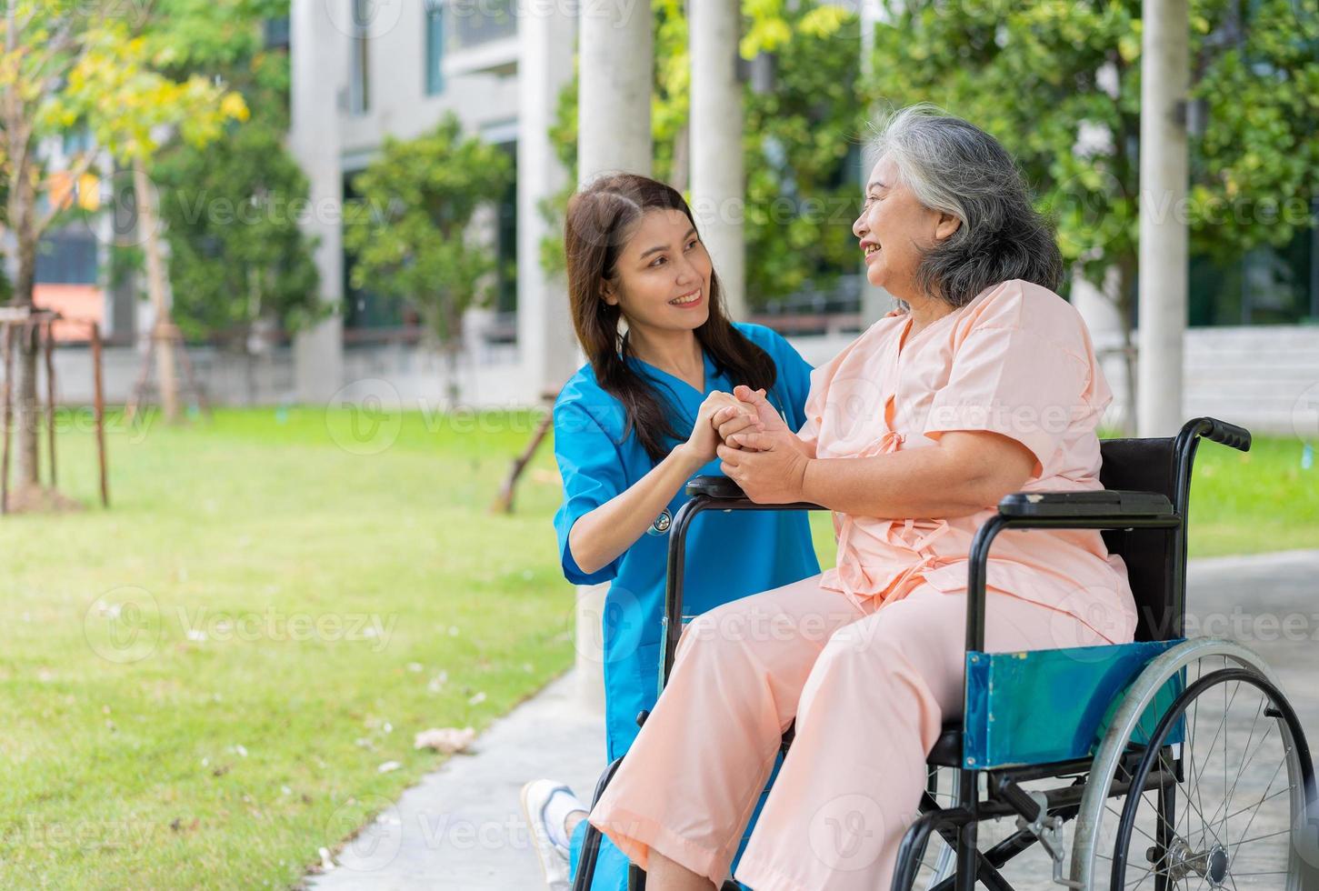 asiatisk omsorgsfull vårdgivare eller sjuksköterska håller patientens hand och uppmuntrar patienten i rullstol. begreppet lycklig pensionering med omsorg från en vårdgivare och sparande och senior sjukförsäkring. foto