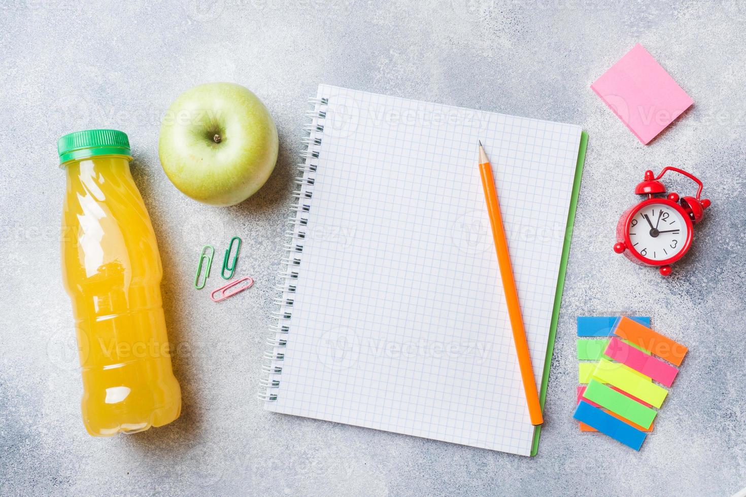 skolmaterial och frukostkex, apelsinjuice och färskt äpple på det grå bordet med kopieringsutrymme. konceptskola. foto