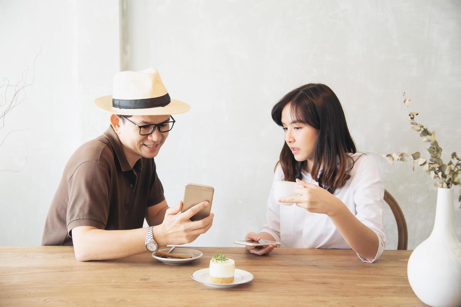 Casual man och kvinna pratar glatt medan de dricker kaffe och tittar på mobiltelefonen - lycklig livsstil i kaféet foto