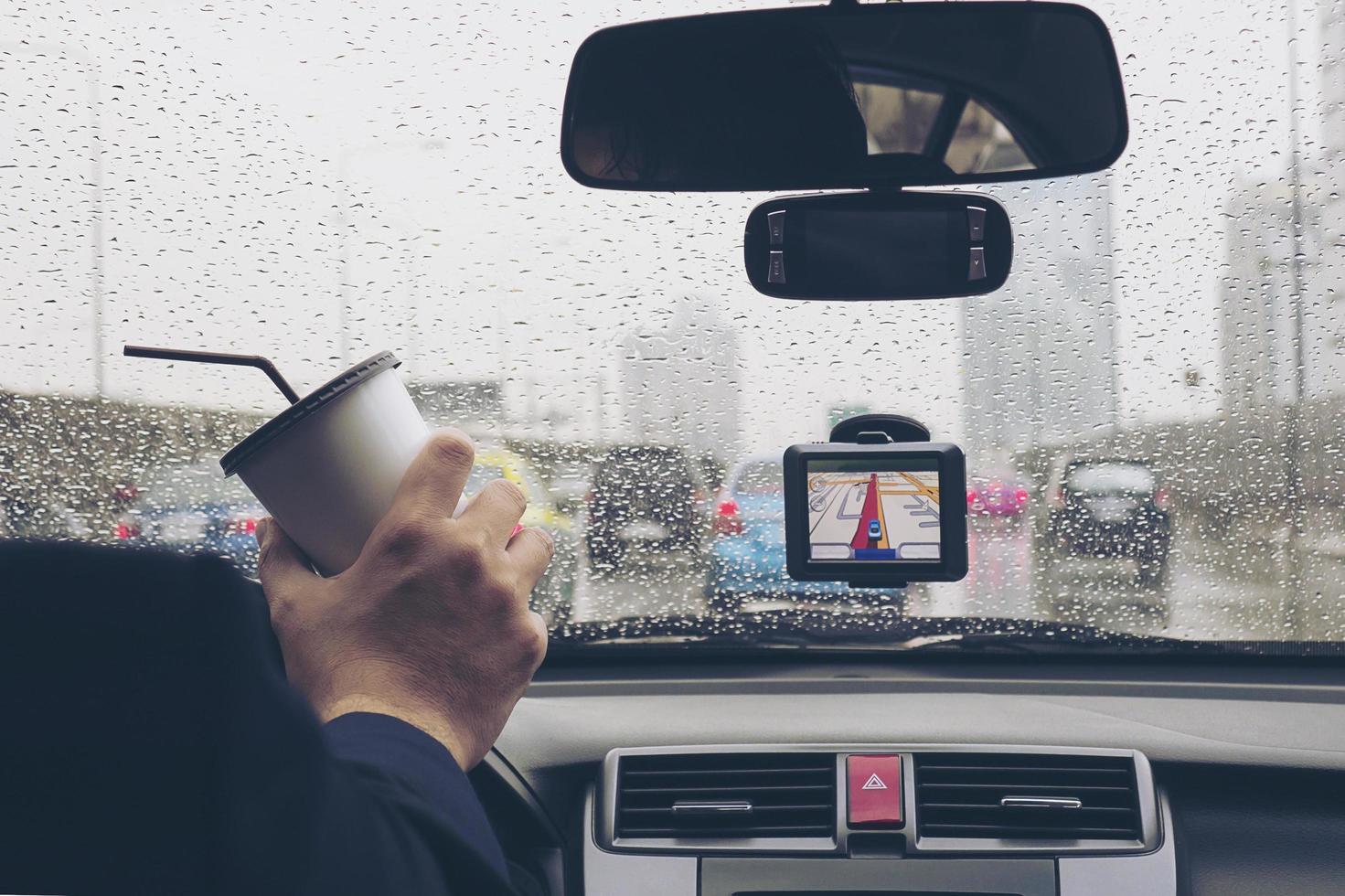 man kör bil med navigatorn och håller kaffekoppen i regnig dag foto