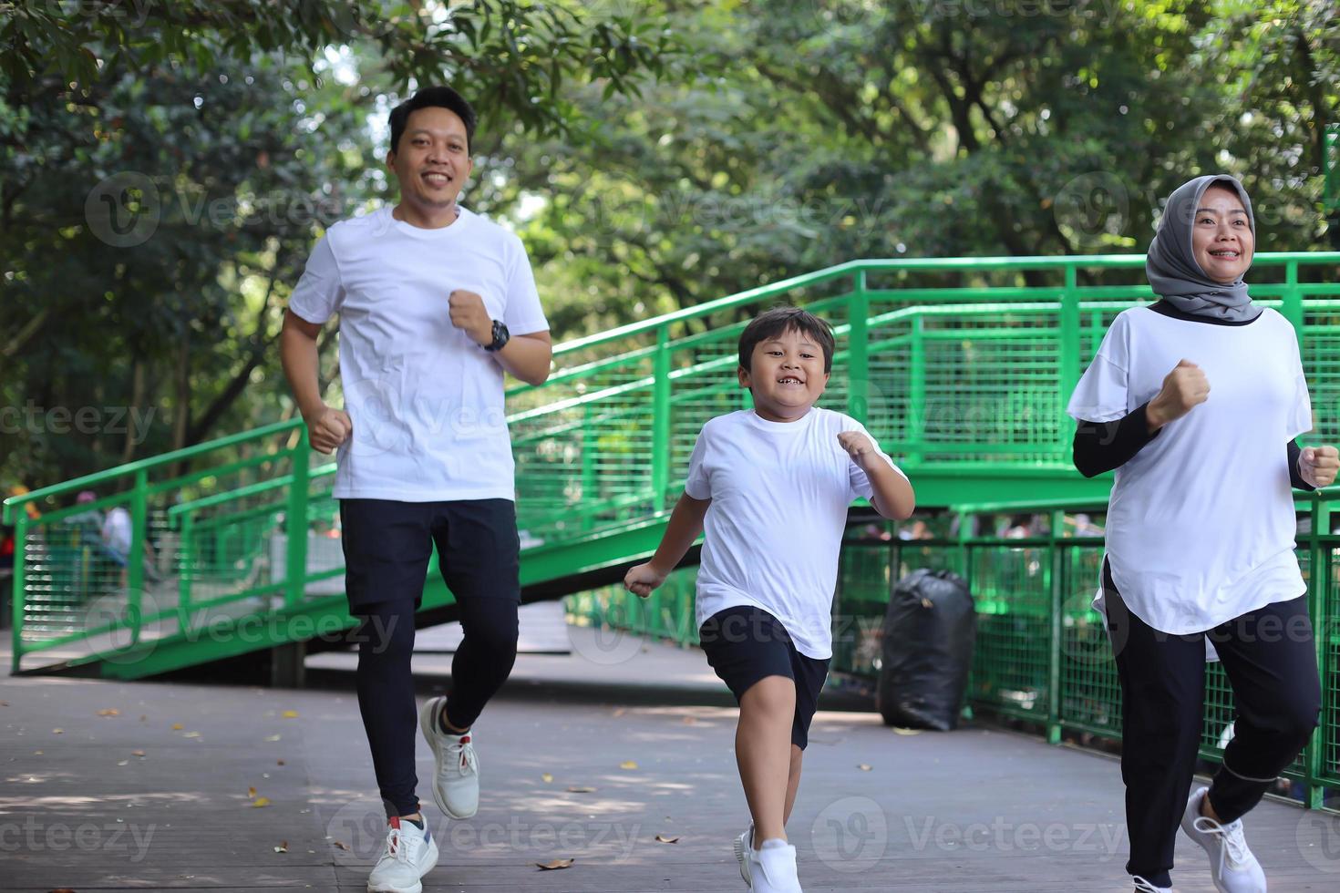 glad asiatisk mamma, pappa och liten pojke springer och spelar fångstspel i grön park. familj, föräldraskap, fritid och människor koncept. foto