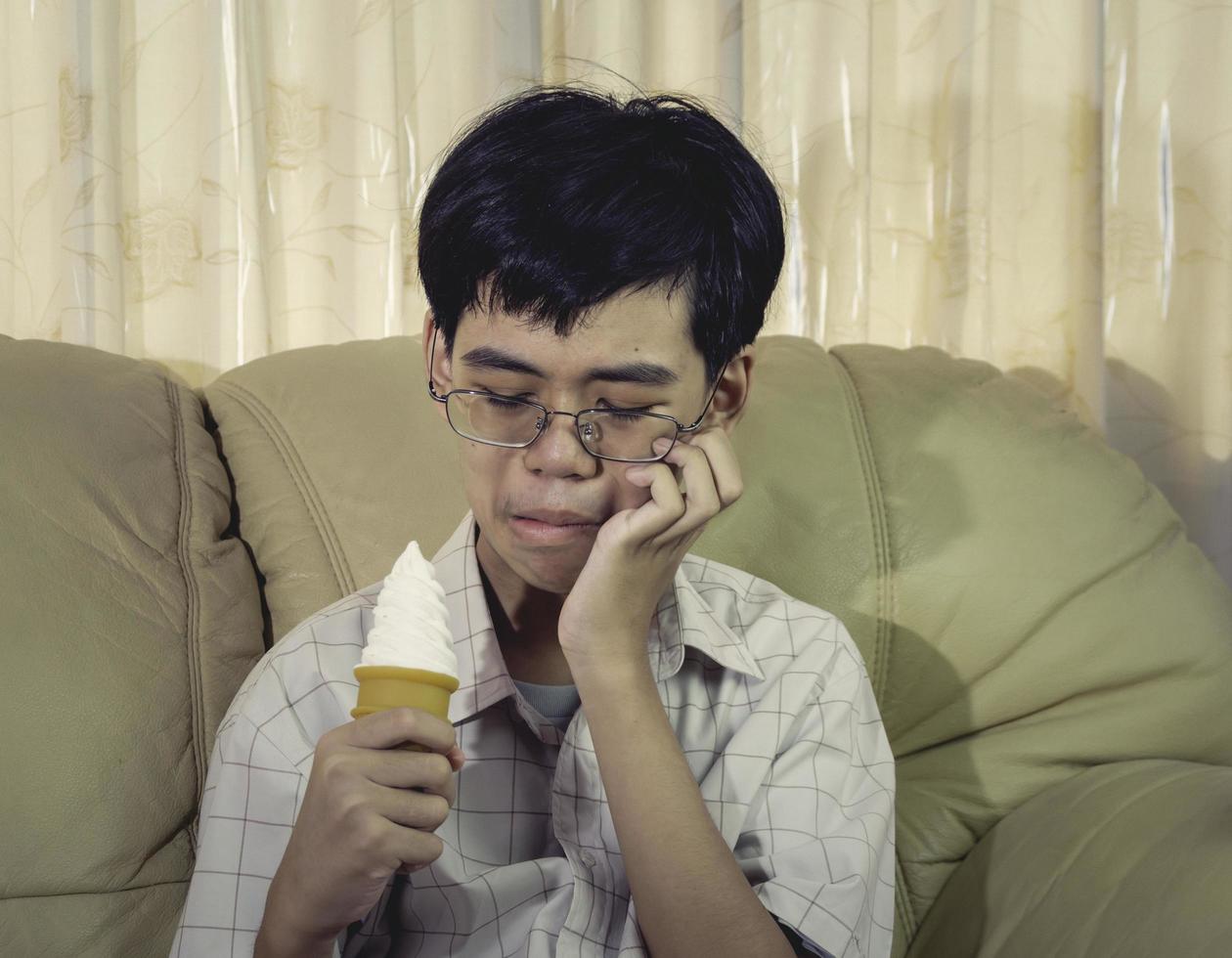 asiatisk ung man med känsliga tänder och kall glass eftersom han äter glass i vardagsrummet. foto