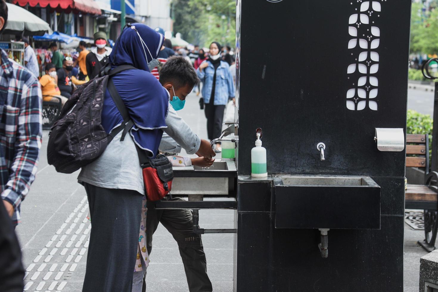 yogyakarta, indonesien - maj 2022 mamma och son tvättar händerna med hjälp av handtvätt på malioboro street. foto