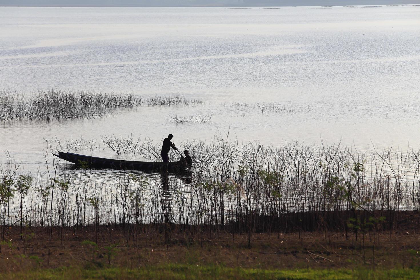 siluett av fiskare på träbåt vid sjön. foto