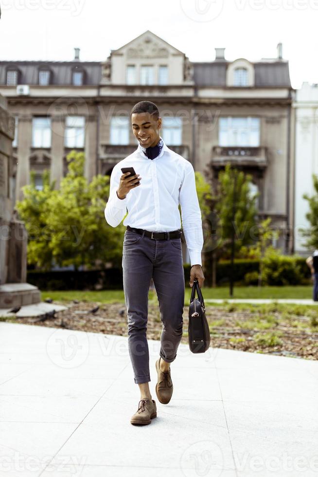ung afroamerikansk affärsman som använder en mobiltelefon medan han går på en gata foto