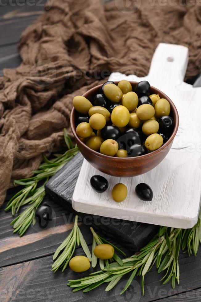 svarta och gröna oliver på en mörk trä rustik bakgrund. foto