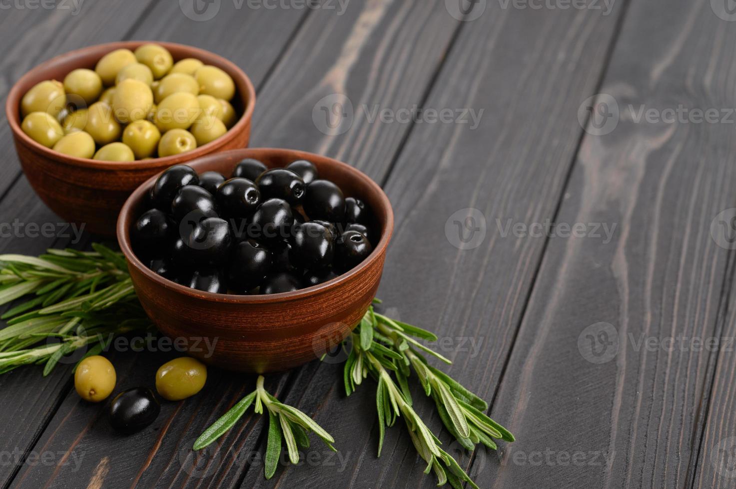 svarta och gröna oliver på en mörk trä rustik bakgrund. foto