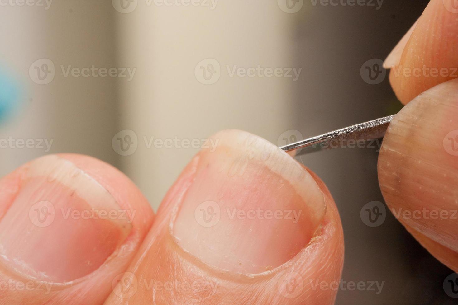 man som rengör sina naglar med en liten metallfil foto