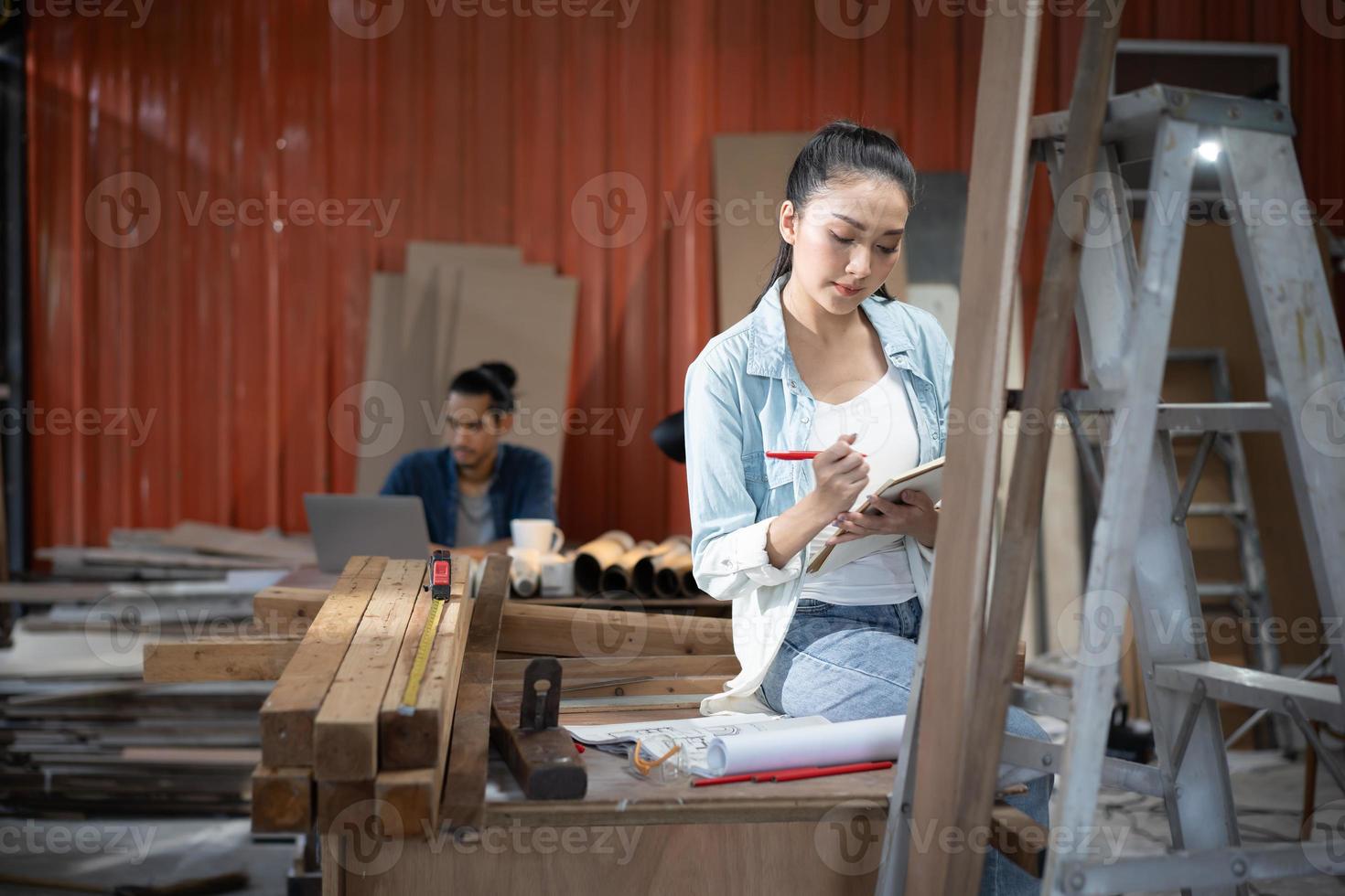 ung asiatisk designmöbler kvinna snickare använder ett måttband för att mäta stol på arbetsbänken i träsnickeri verkstad. foto