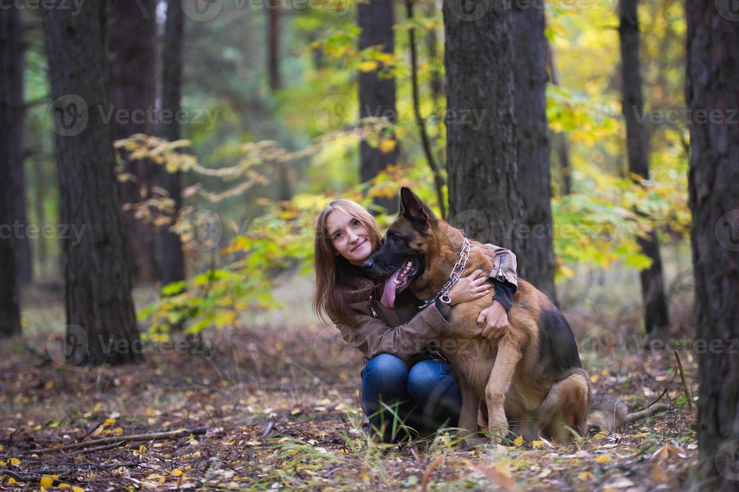 ung söt kvinna kramar en schäferhund utomhus i höstskogen foto