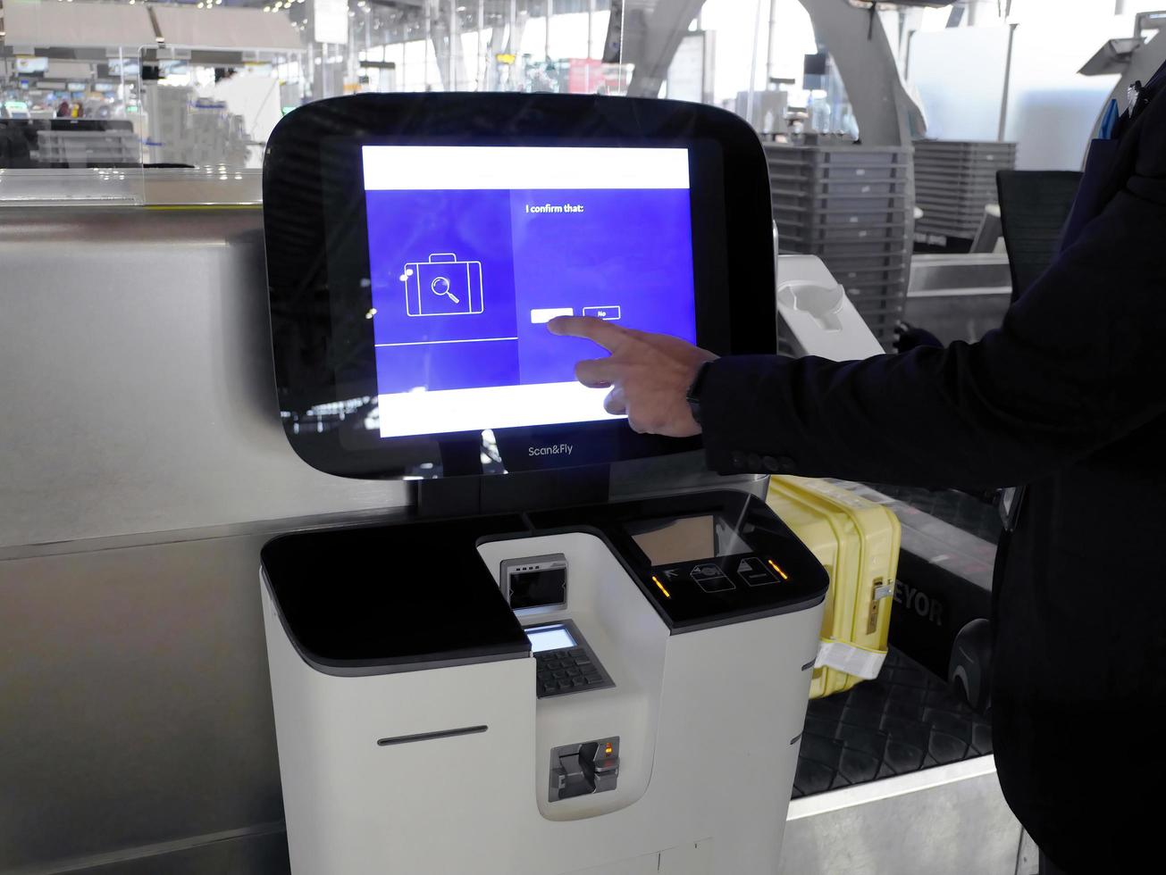 en hand som trycker på monitorn, självincheckningsmaskin på bangkoks internationella flygplats, lastning av bagage, self bag drop och få boardingkortet. foto