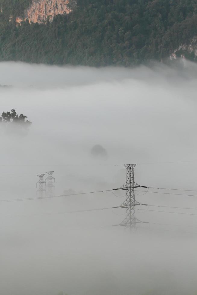 elektriska kraftledningar och pyloner som dyker upp ur dimman foto