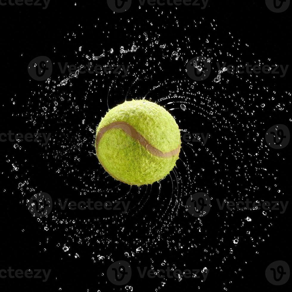 tennisboll snurrar snabbt stänk vattendroppar i en cirkel på svart bakgrund. foto
