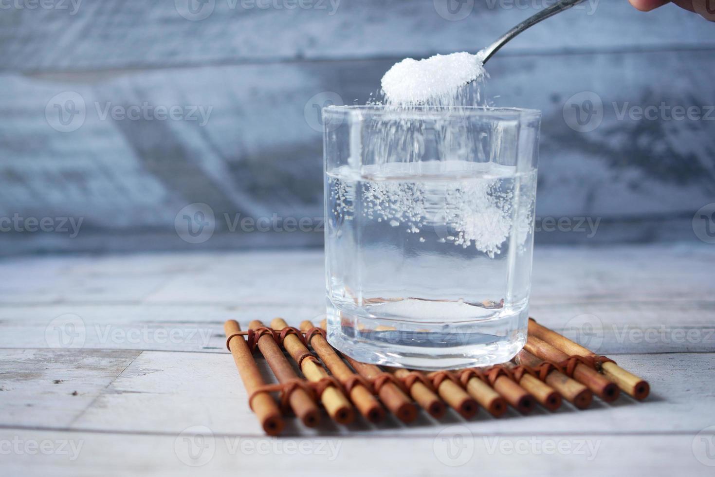 hälla vitt socker i ett glas vatten på bordet foto