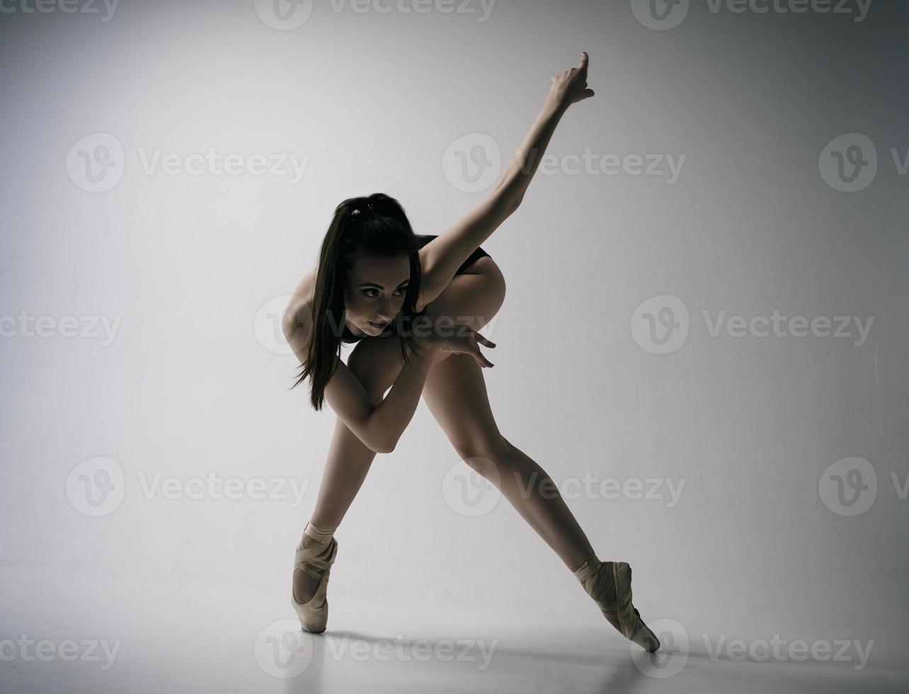 en ballerina i bodysuit och en vit kjol improviserar klassisk och modern koreografi i en fotostudio foto