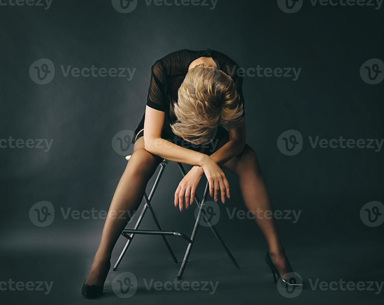 trött blond kvinna sitter på en stol med armarna i kors och huvudet sänkt i känslor av förtvivlan och sorg foto