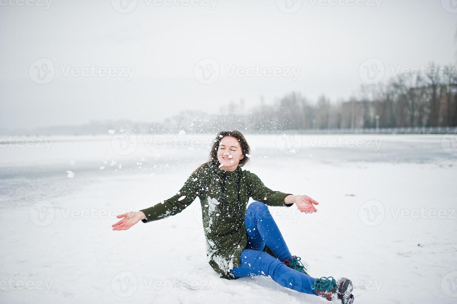 rolig flicka slitage på lång grön tröja och jeans, vid frusen sjö i vinterdag. foto