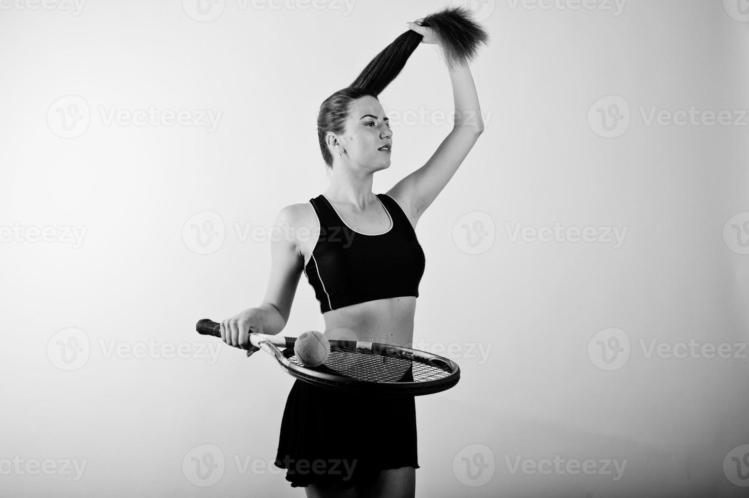 svart och vitt porträtt av vacker ung kvinna spelare i sportkläder håller tennisracket medan stående mot vit bakgrund. foto