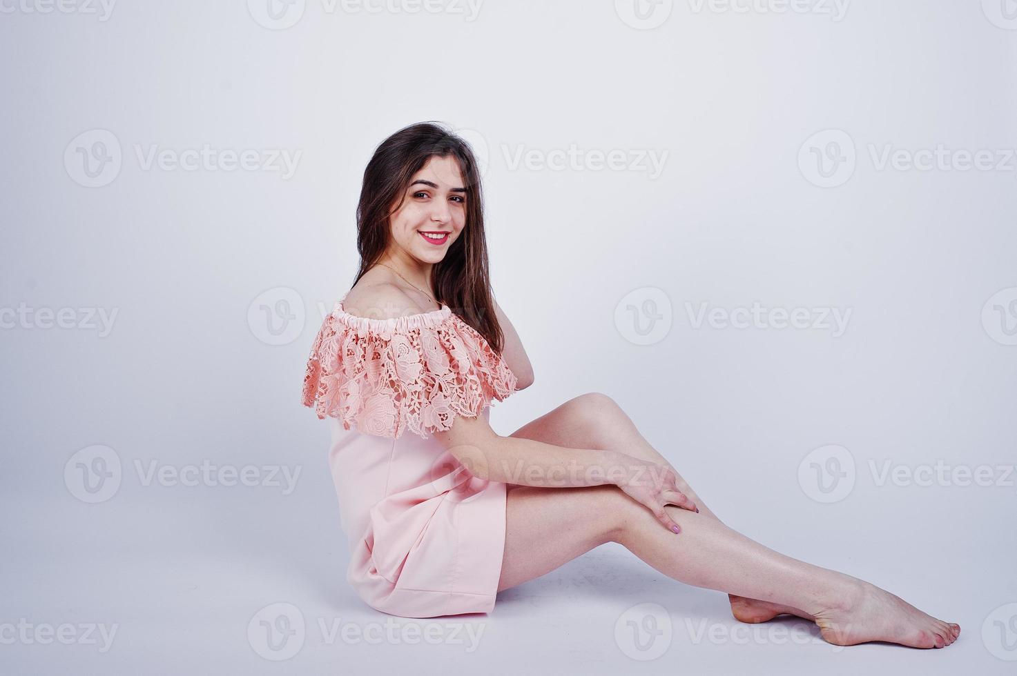 porträtt av en fashionabel kvinna i rosa klänning som sitter och poserar på golvet i studion. foto