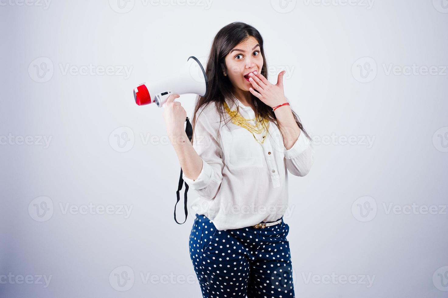 porträtt av en ung kvinna i blå byxor och vit blus poserar med megafon i studion. foto