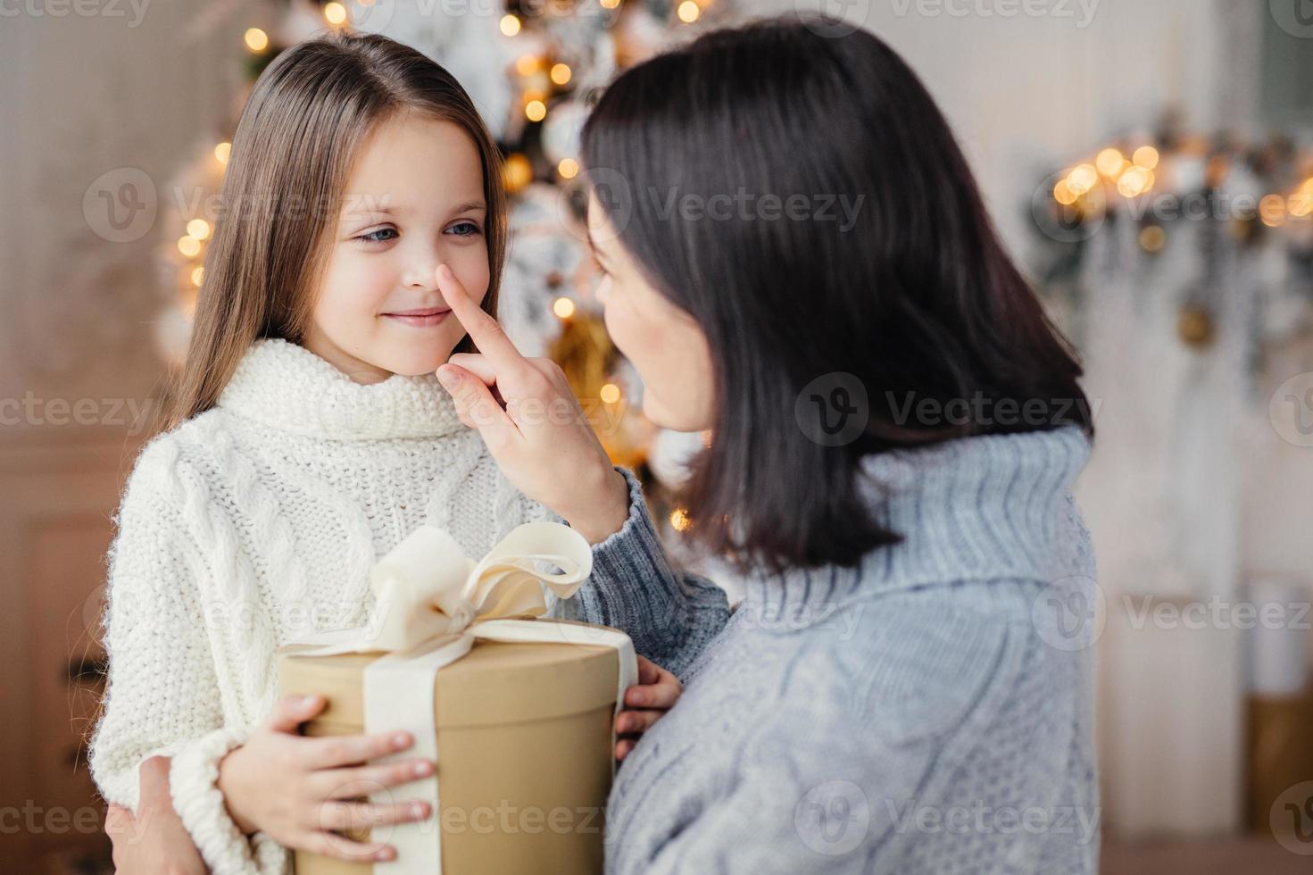 tillgiven mamma ger present till sin bedårande lilla dotter, förbereder överraskning på jul, rör vid hennes näsa, uttrycker stor kärlek. familj, firande, presenter, mirakel, vinter semester koncept foto