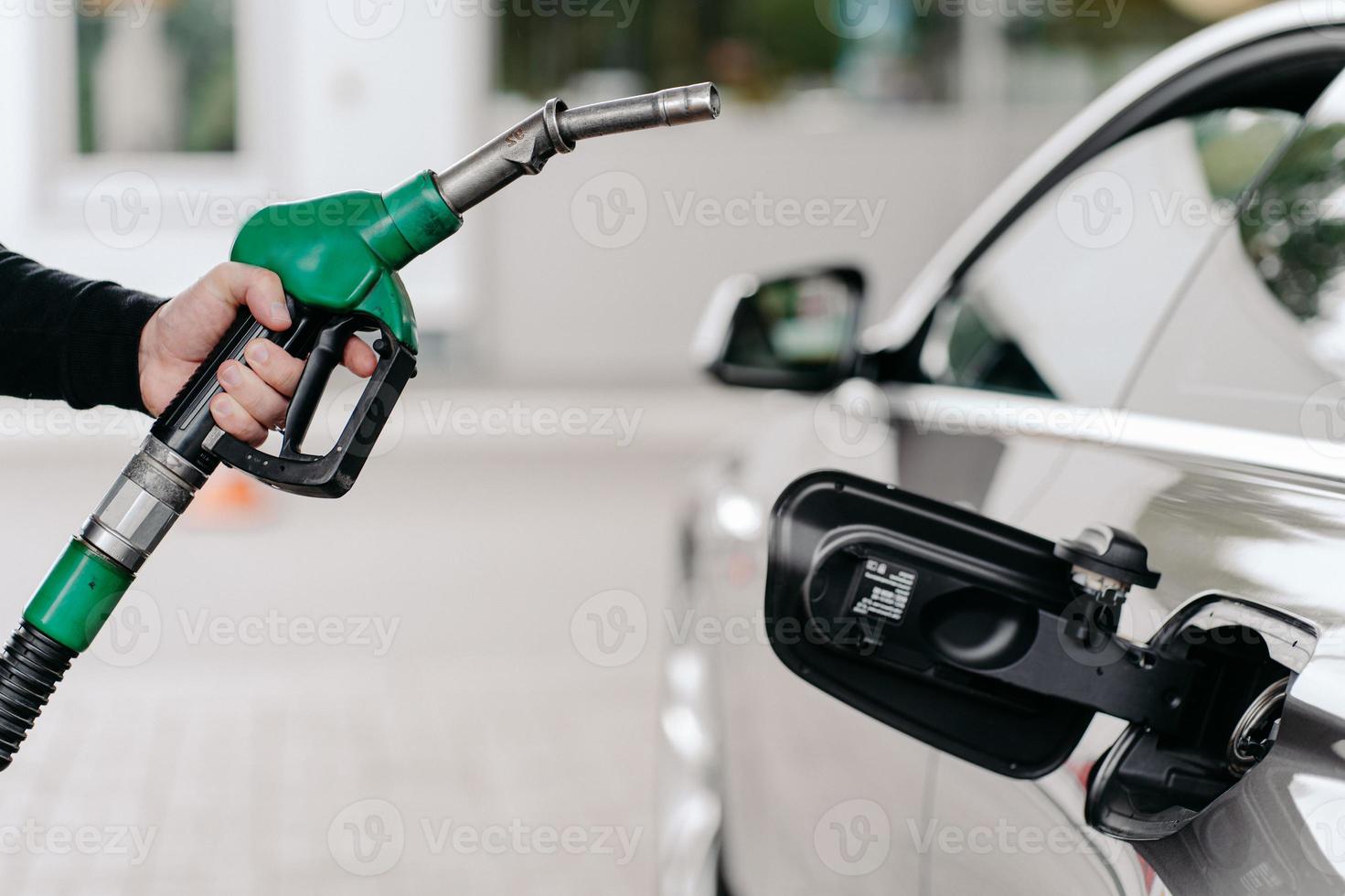beskuren bild av mans hand som pumpar bensin i bilen på bensinstationen. bilen fylls med bensin. oigenkännlig man håller bränslemunstycke. foto