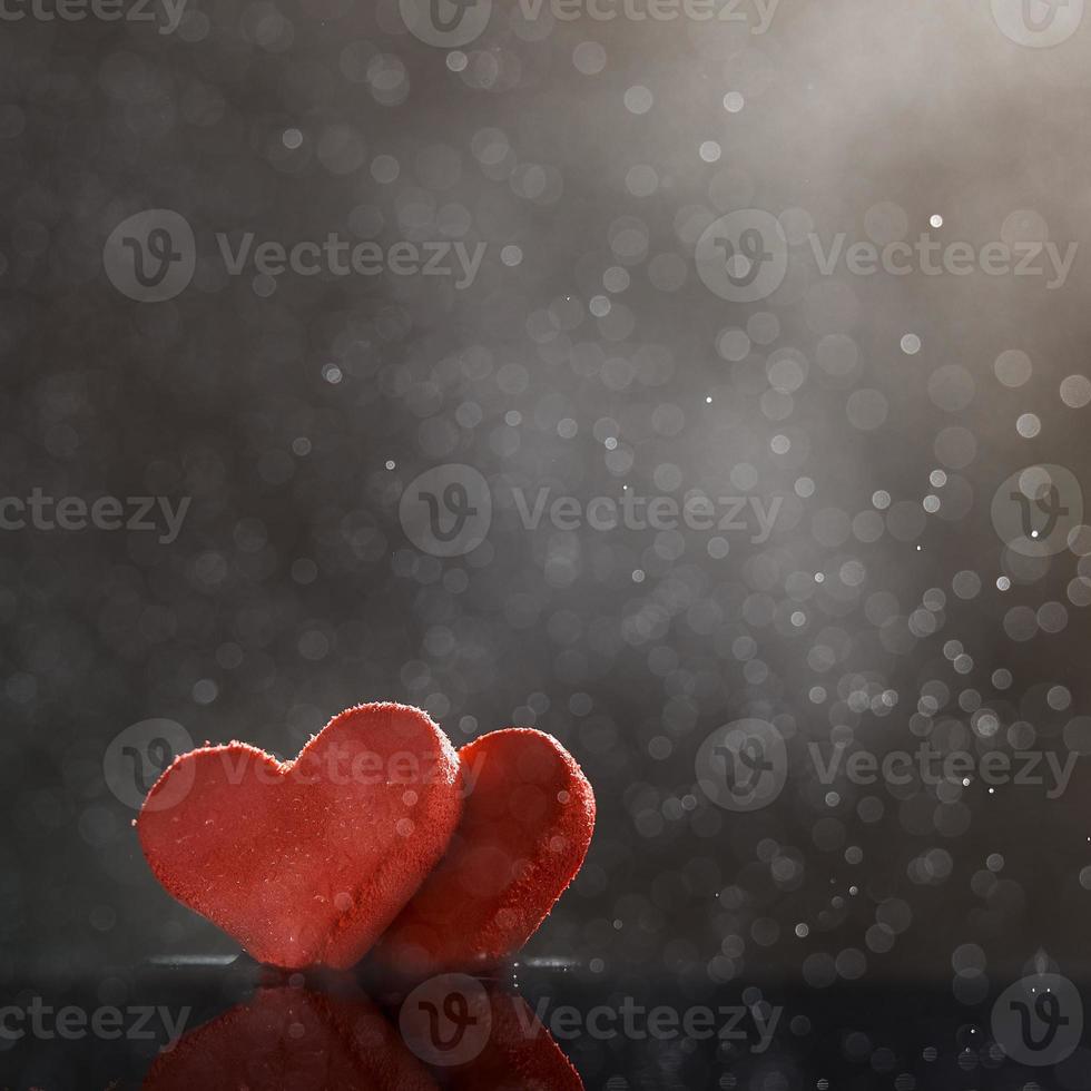 två röda hjärtan med regndroppar upplysta av varmt ljus på mörk bakgrund med en bokeh. foto med kopia utrymme.
