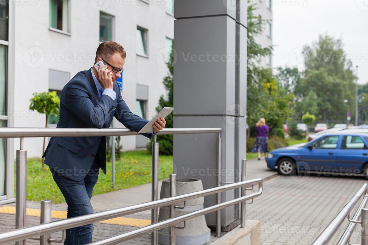 kaukasiska affärsman utanför kontoret använder mobiltelefon och surfplatta. foto