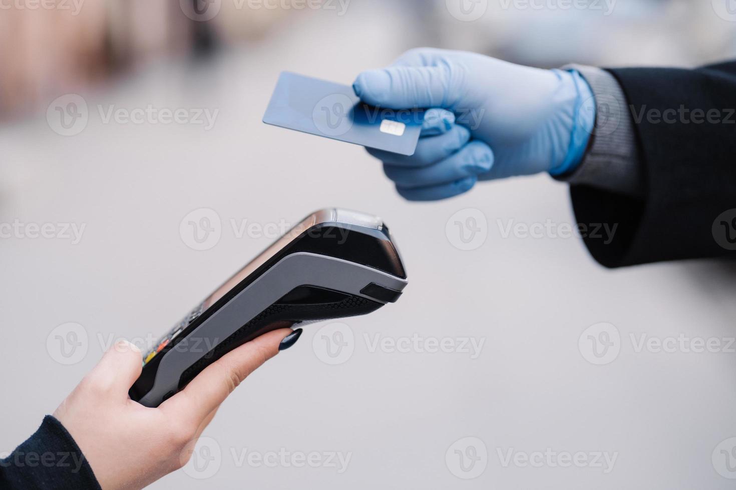 ansiktslös människa i medicinska handskar under coronavirusepidemin, håller plastkort, försöker göra kontantlös betalning för säkerhets skull, använder modern teknik. pandemi, virus och förebyggande koncept foto