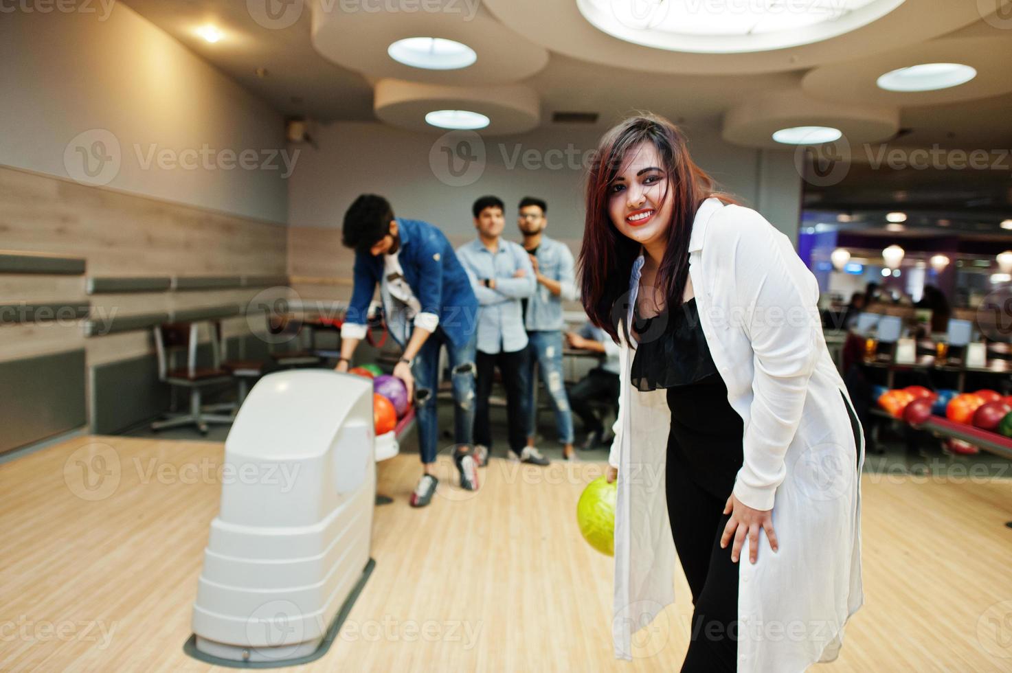 sydasiatisk kvinna står vid bowlinghall med boll på händerna. flickan förbereder sig för ett kast. foto