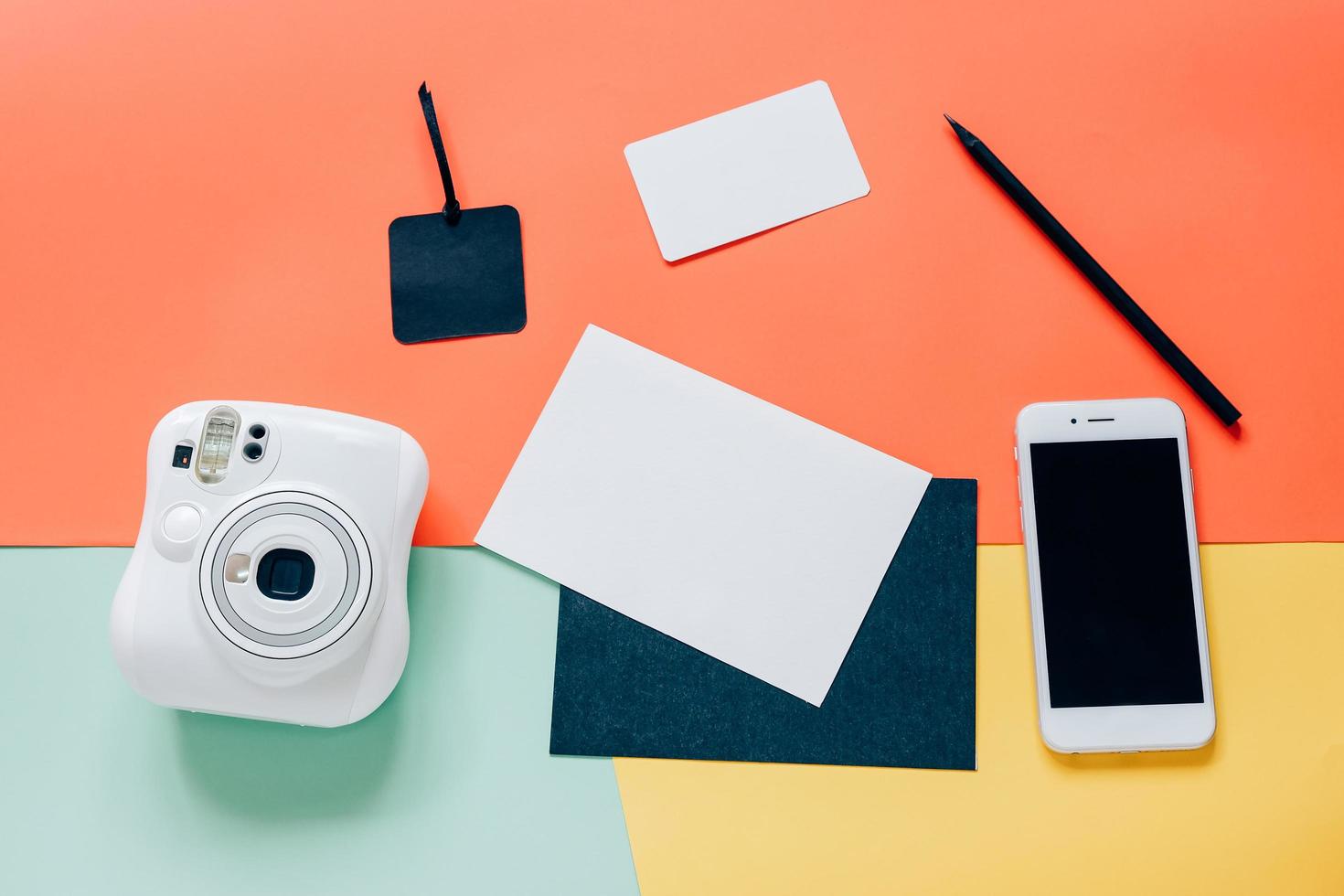 kreativ platt liggande stil på skrivbordet med omedelbar kamera, smartphone, tomt kort, tagg och penna på minimal färgbakgrund foto