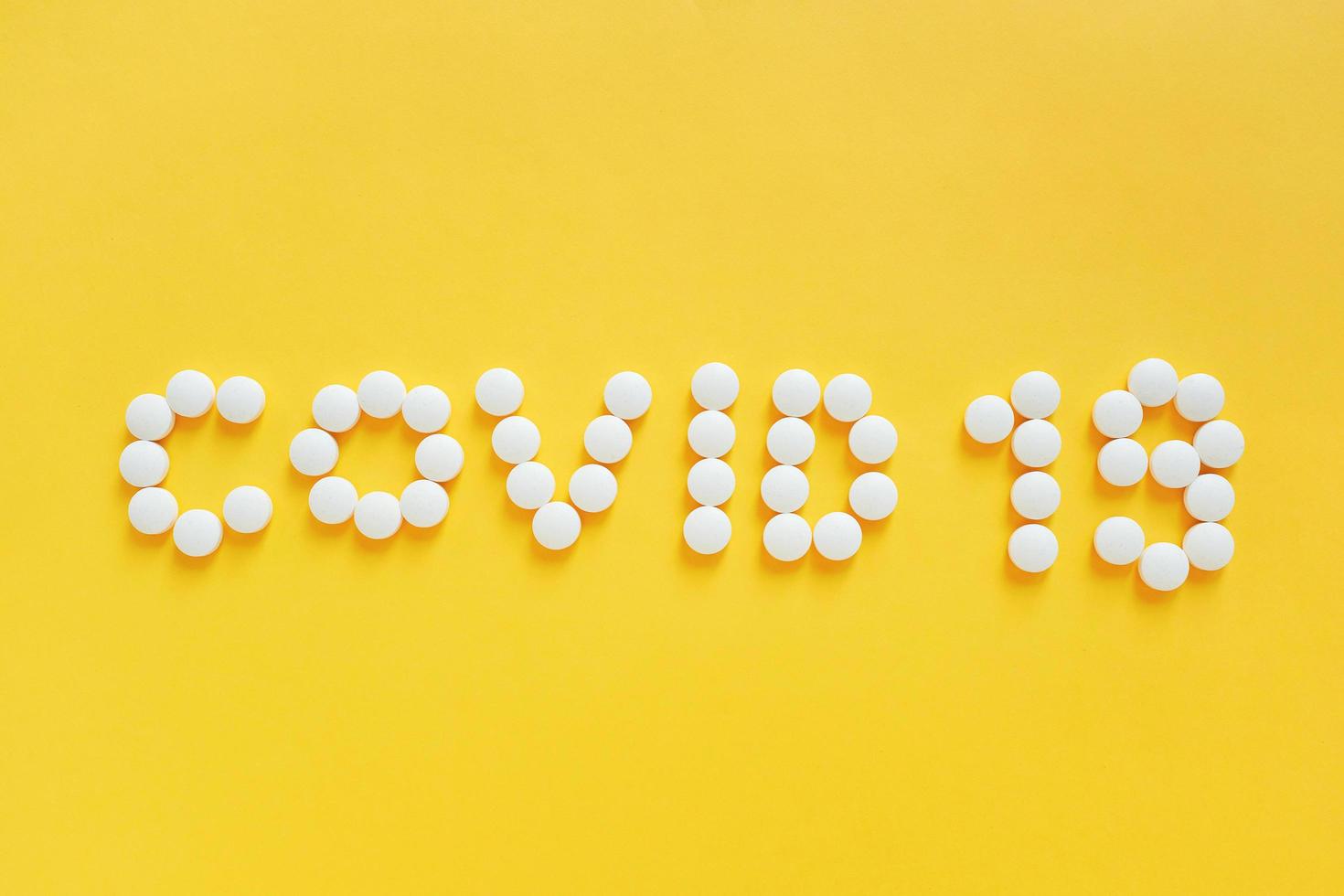 platt läggning av medicinpiller formar som ordet covid 19 på gul bakgrund, hälsovårdskoncept och förhindrar spridningen av pandemi covid-19 och coronavirus foto