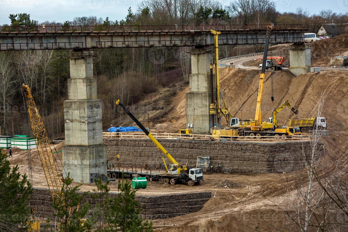 konstruktion eller rekonstruktion av motorvägsbetongbro över en bred flod. anläggningsmaskiner, lastbilar och kranar fungerar foto