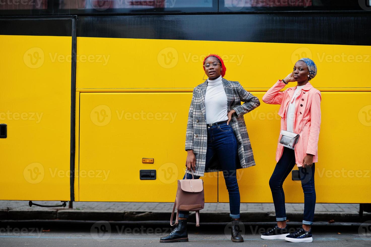 två unga moderna fashionabla, attraktiva, långa och smala afrikanska muslimska kvinnor i hijab eller turban huvudduk och kappa poserade mot gul buss. foto