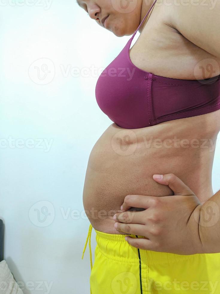 fet asiatisk kvinna som står i sidled visar sin mage foto
