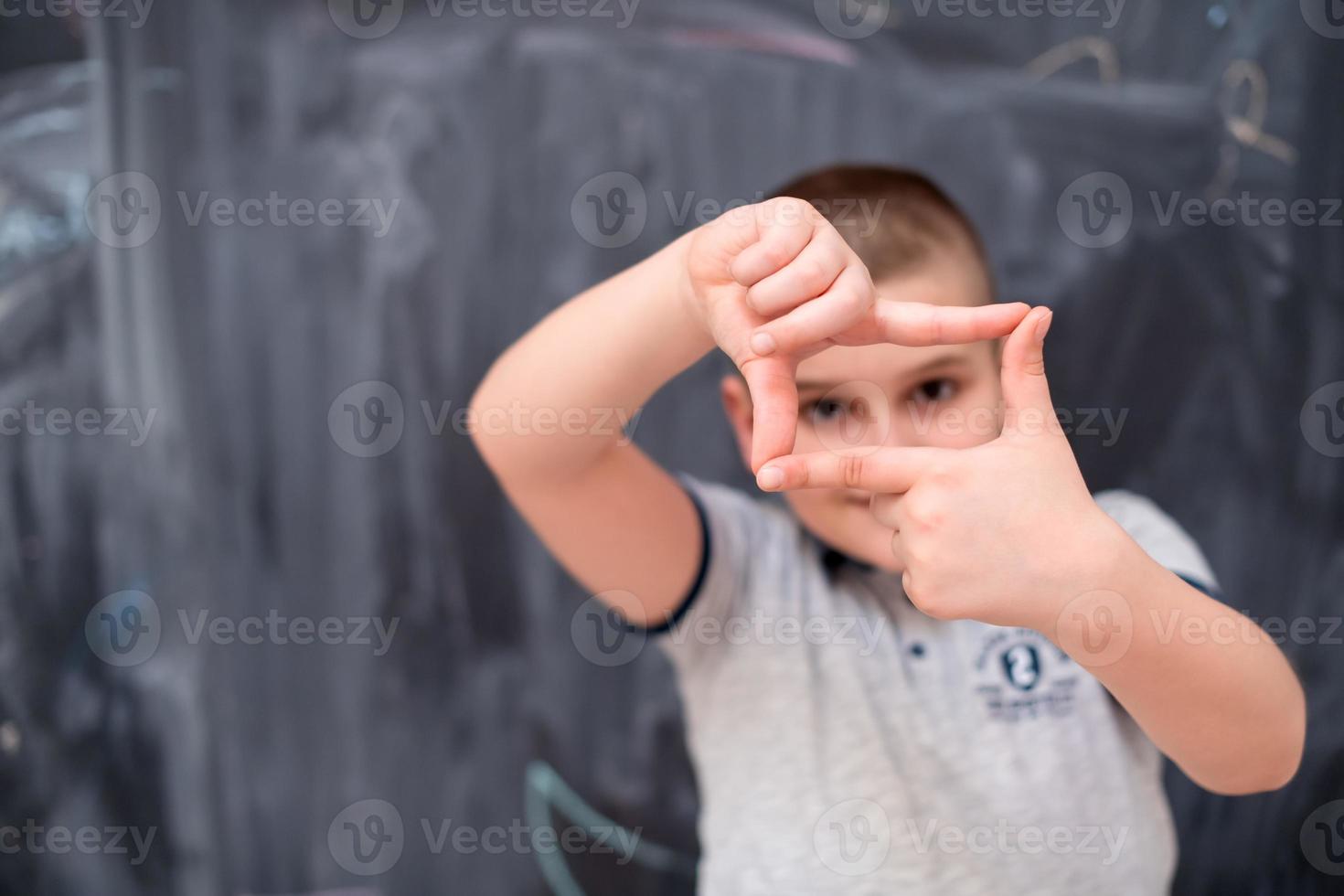 glad pojke gör hand ram gest framför svarta tavlan foto