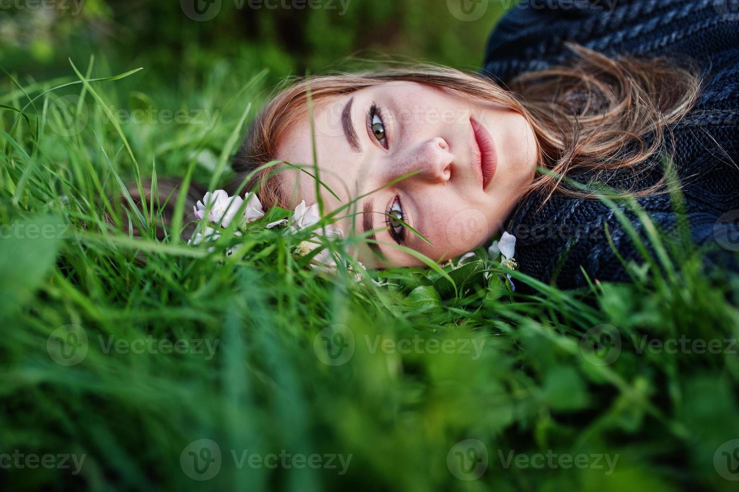 ung brunett flicka liggande på grönt gräs med grenar av blomma träd. foto